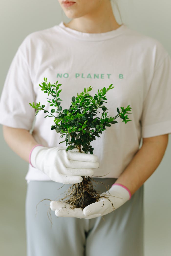 Woman wearing gloves holds a plant with 'No Planet B' shirt, promoting eco-friendly lifestyle.